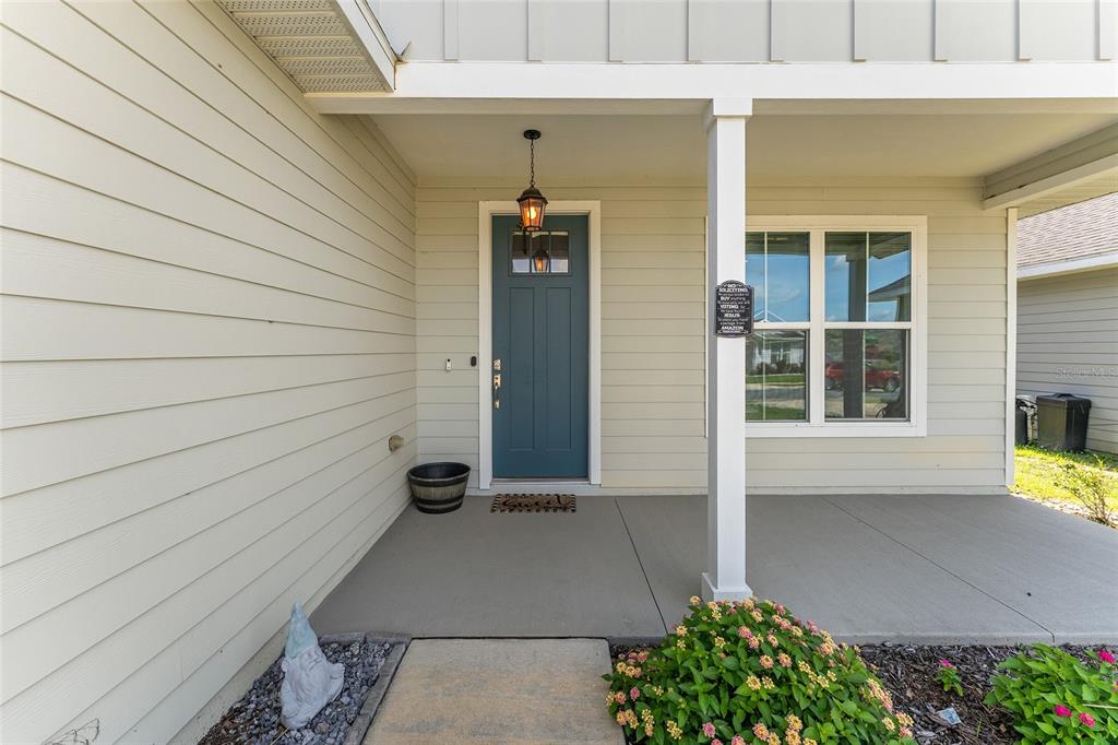 A covered front porch features a blue door, a gnome statue, and a small garden — 12327 NW 159TH WAY, ALACHUA, FL
