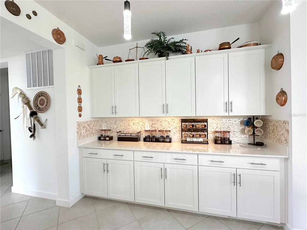 A kitchen features white cabinets, a light-colored countertop, and a tiled backsplash with decorative accents — 8608 SAINT KITTS CIRCLE, ENGLEWOOD, FL