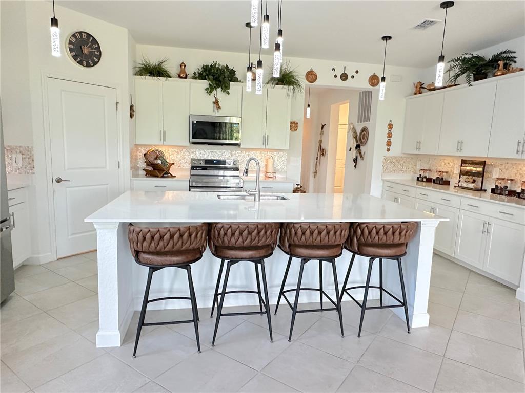 A kitchen features a large white island with four brown stools and white cabinetry — 8608 SAINT KITTS CIRCLE, ENGLEWOOD, FL