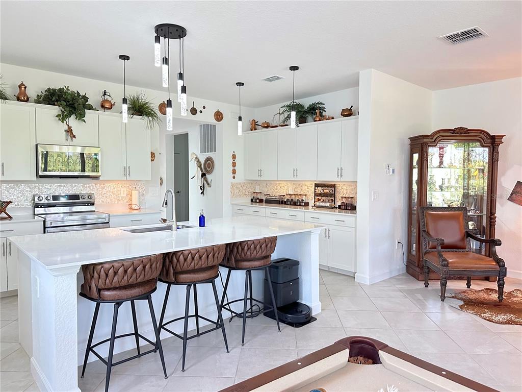 A modern kitchen features white cabinetry, a large island with bar stools, and tile flooring — 8608 SAINT KITTS CIRCLE, ENGLEWOOD, FL