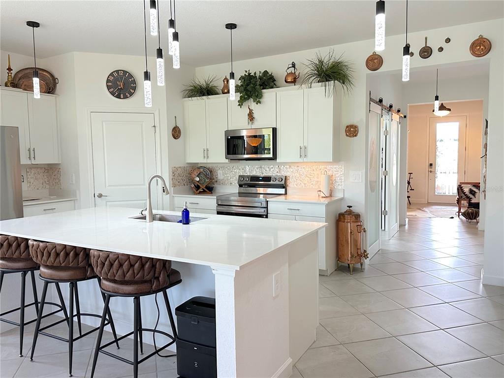 A kitchen features white cabinetry, a central island with bar stools, and tiled flooring — 8608 SAINT KITTS CIRCLE, ENGLEWOOD, FL