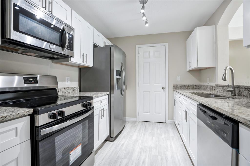 A kitchen features white cabinets, stainless steel appliances, granite countertops, and light wood-look flooring — 3960 SOUTHPOINTE DRIVE UNIT 504, ORLANDO, FL