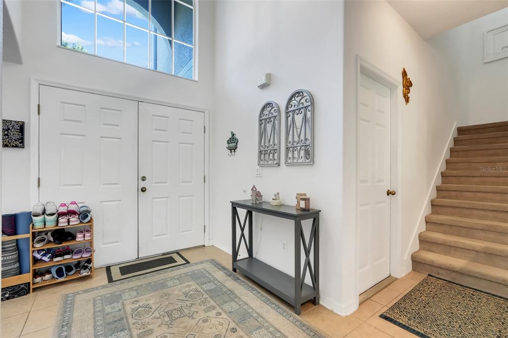 An entryway features a high ceiling, double front doors, a staircase, and a console table — 12608 WEATHERFORD WAY, ORLANDO, FL