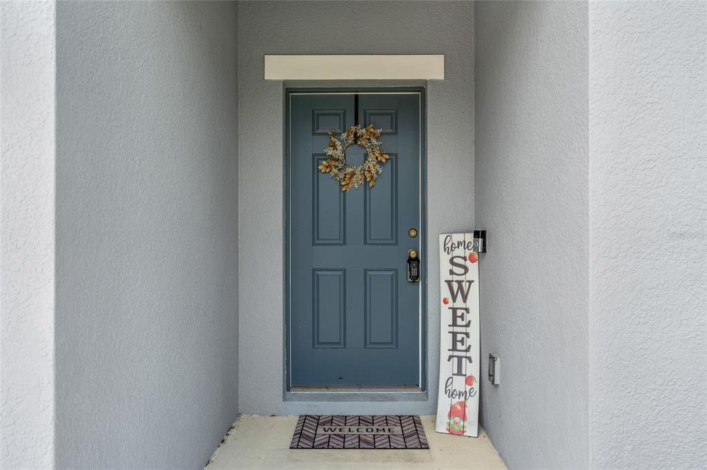 A blue front door with a wreath, a welcome mat, and a decorative sign — 87 PRAIRIE FALCON DRIVE, GROVELAND, FL