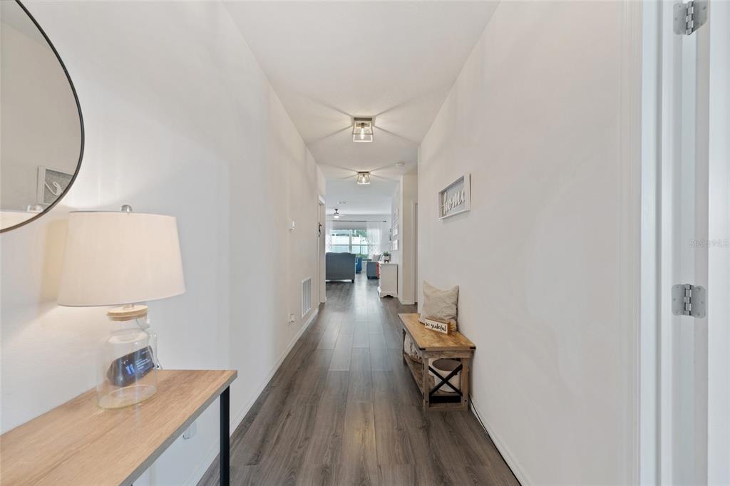 A hallway with wood-look flooring leads from a foreground console table toward a living area — 87 PRAIRIE FALCON DRIVE, GROVELAND, FL