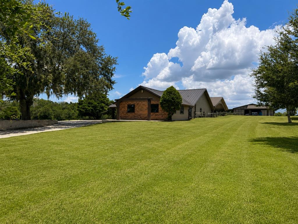 A large, single-story house with a brick facade and metal roof sits on a grassy lawn — 6820 COUNTY ROAD 561, CLERMONT, FL