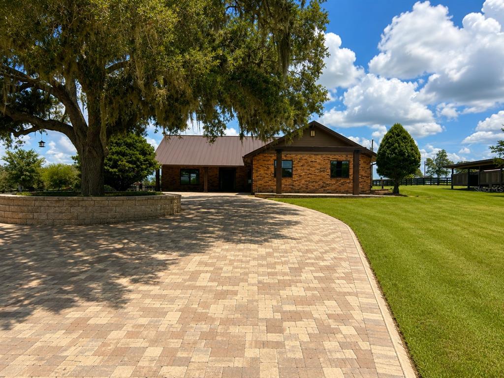 A brick house with a metal roof and a large paver driveway under a tree — 6820 COUNTY ROAD 561, CLERMONT, FL