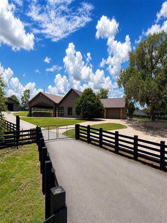 A paved driveway leads to a house with a metal roof and black wooden fencing — 6820 COUNTY ROAD 561, CLERMONT, FL