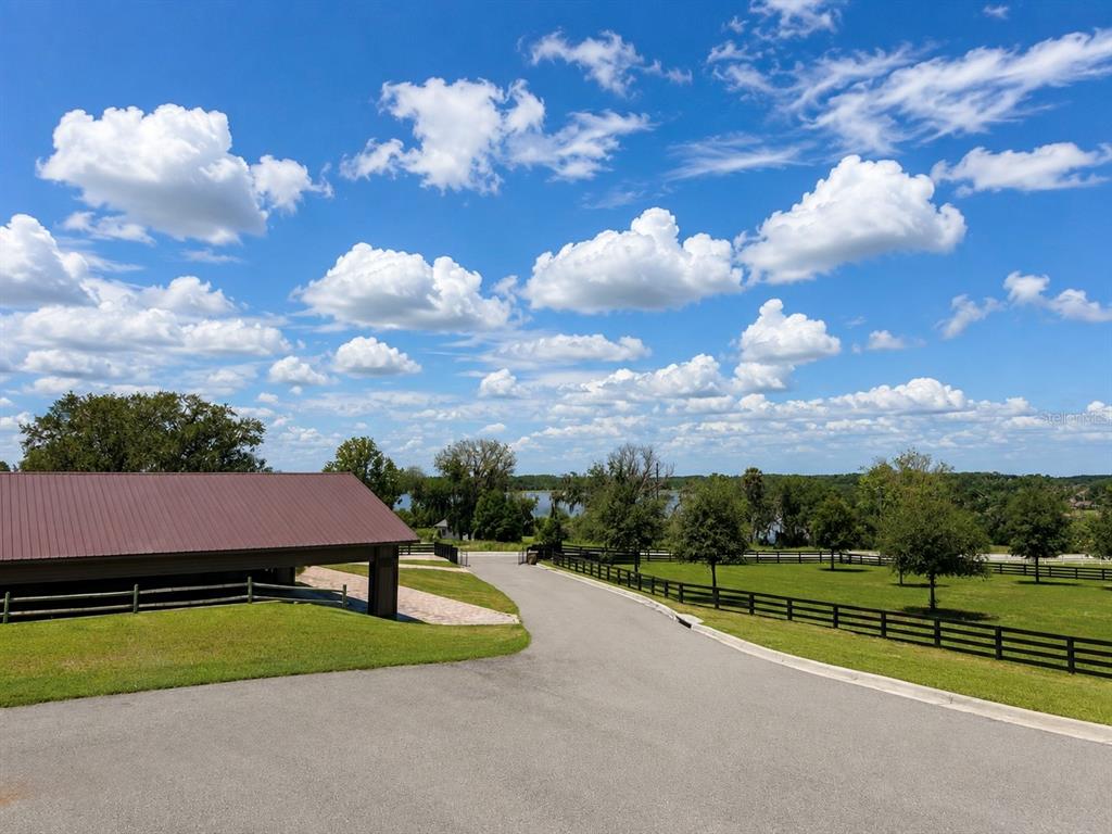 A paved driveway leads past a brown metal-roofed barn toward a grassy field and lake — 6820 COUNTY ROAD 561, CLERMONT, FL