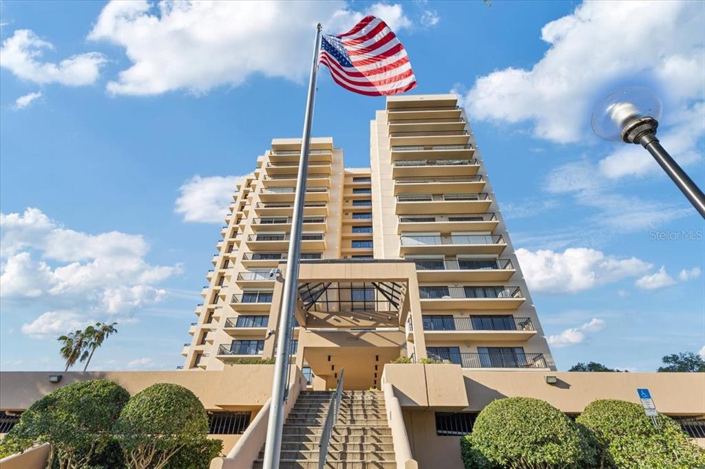 A low-angle view of a multi-story tan apartment building with balconies and an American flag — 7550 HINSON STREET UNIT 15D, ORLANDO, FL