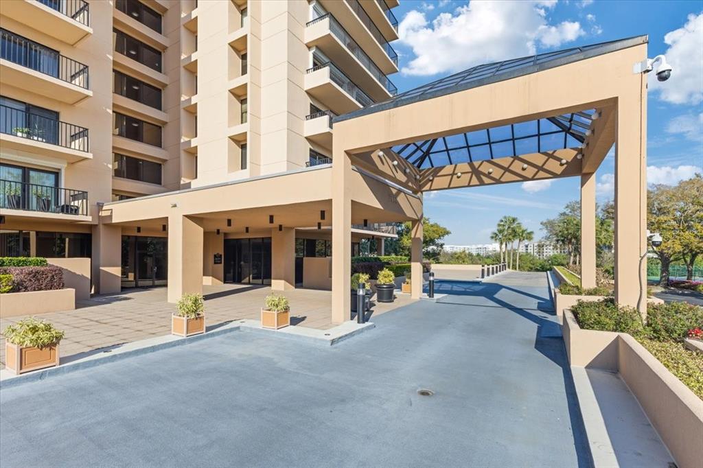 A beige high-rise building features a covered porte-cochère entrance with a glass-paneled roof — 7550 HINSON STREET UNIT 15D, ORLANDO, FL