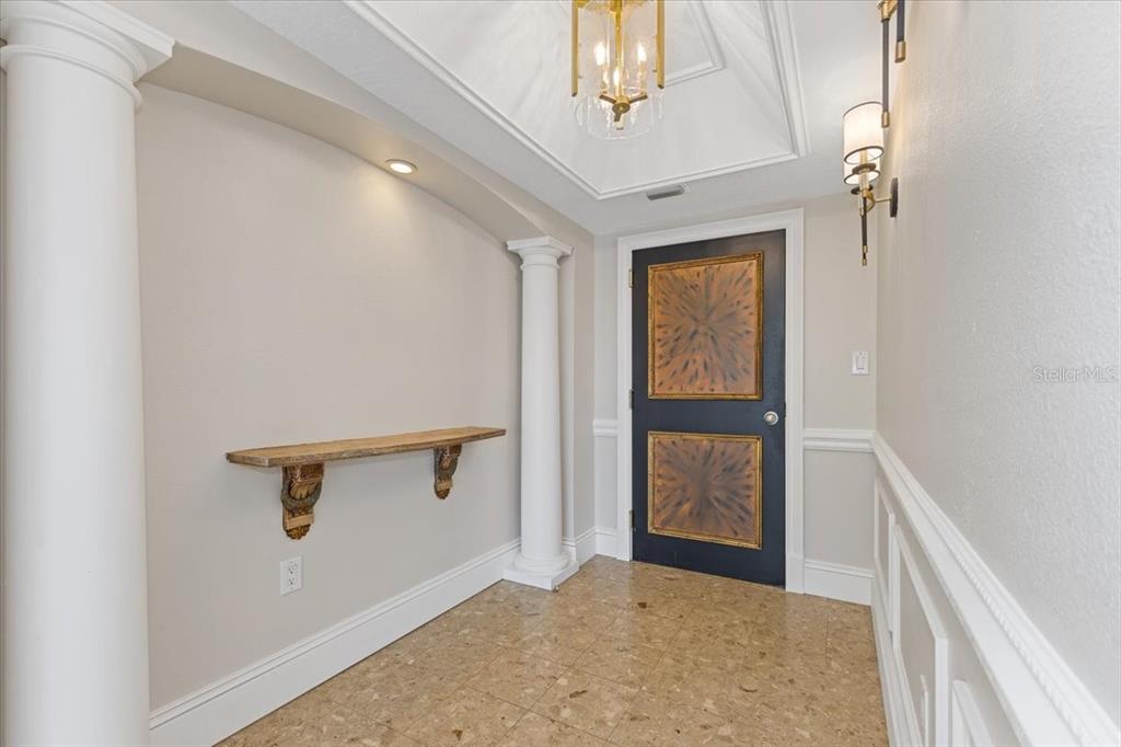 An entryway features a dark door with decorative panels, columns, a wall shelf, and tile flooring — 7550 HINSON STREET UNIT 15D, ORLANDO, FL