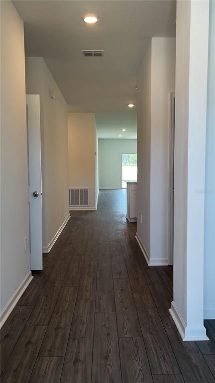 A hallway with dark wood-look tile flooring leads toward an open-concept kitchen and living area — 4844 NW 11TH ST ROAD, OCALA, FL