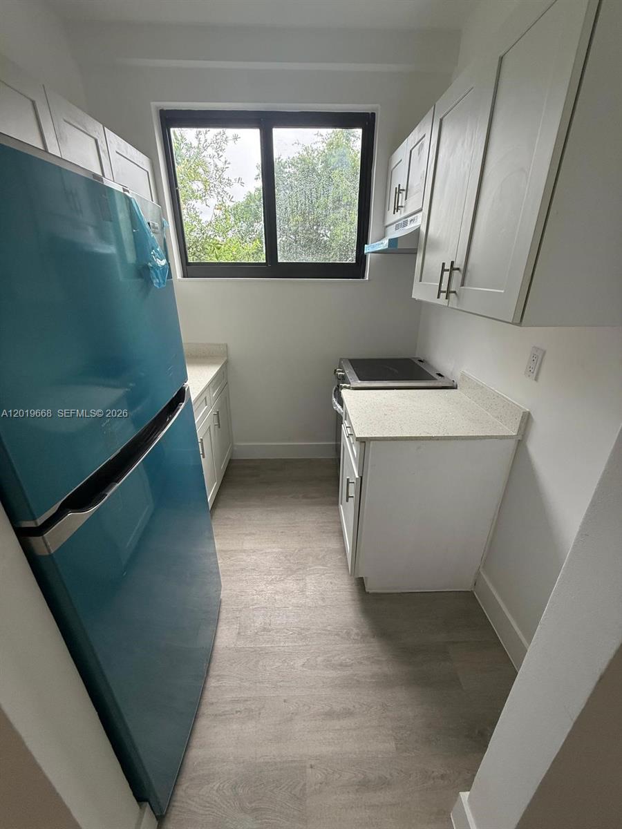 A small galley kitchen features white cabinets, light countertops, a window, and a blue refrigerator — 2330 NW 9 St # 15, Miami FL 33125, MIAMI, FL