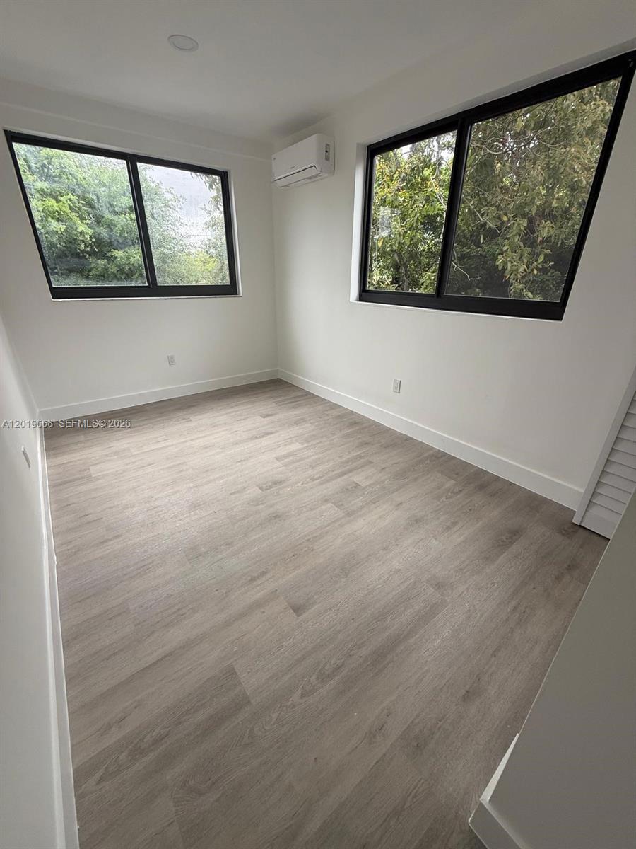A bright, empty bedroom features light wood-look flooring, white walls, and two large windows — 2330 NW 9 St # 15, Miami FL 33125, MIAMI, FL