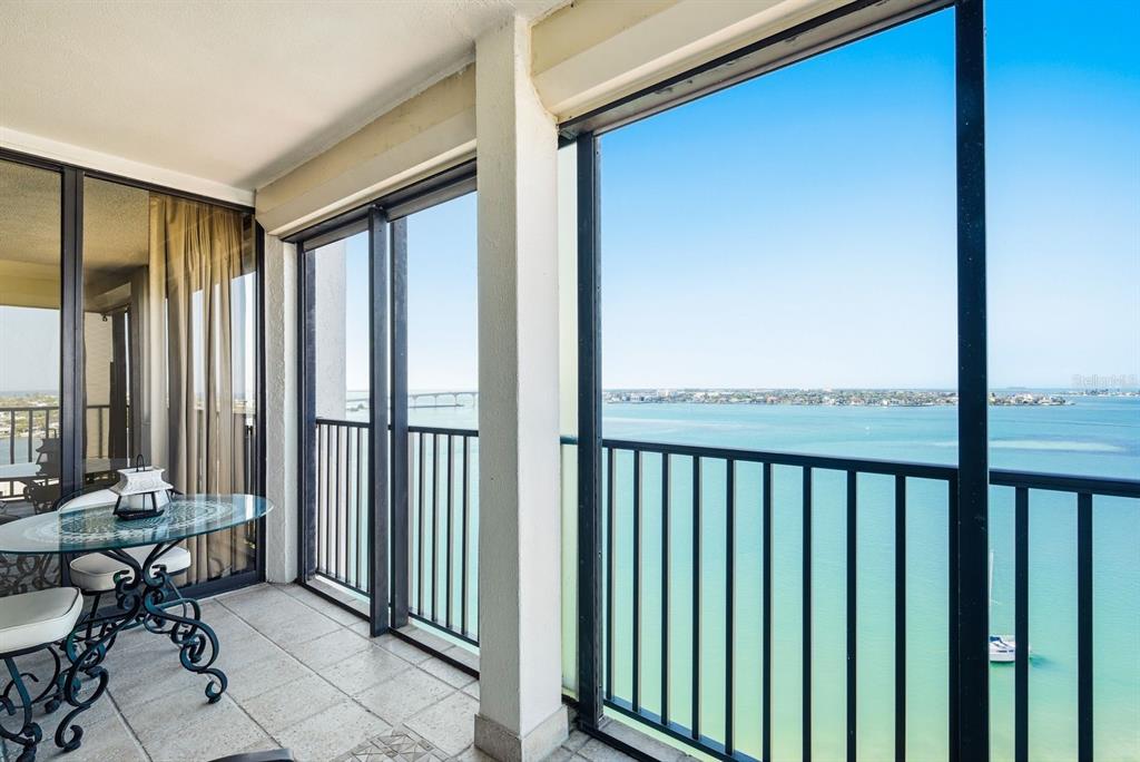 A balcony with a glass table overlooks a large body of water and a bridge — 6287 BAHIA DEL MAR CIRCLE UNIT 1202, ST PETERSBURG, FL