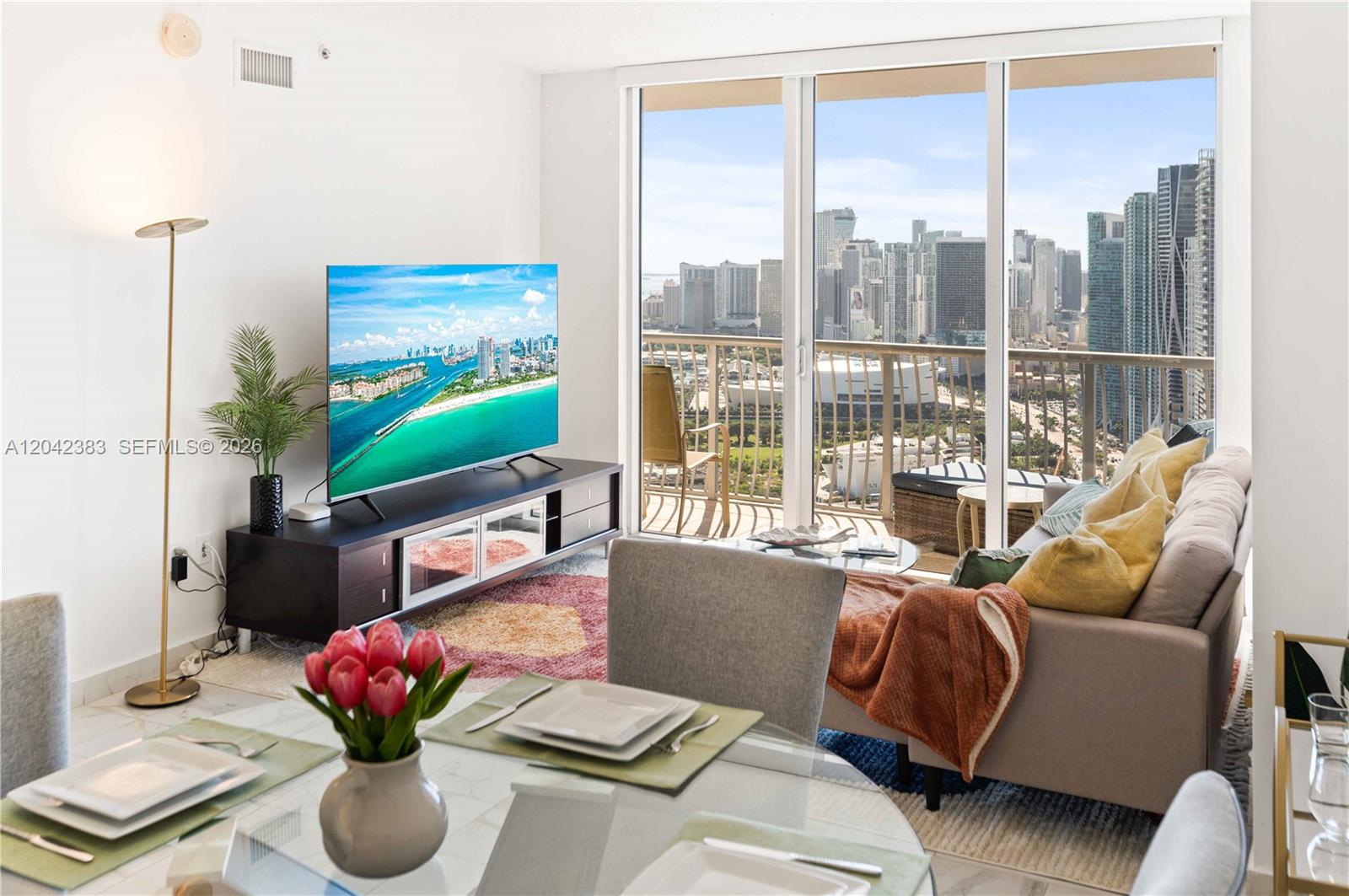 A living room features a television, sofa, and floor-to-ceiling windows overlooking a city skyline — 1750 N Bayshore Dr # 5212, Miami FL 33132, MIAMI, FL