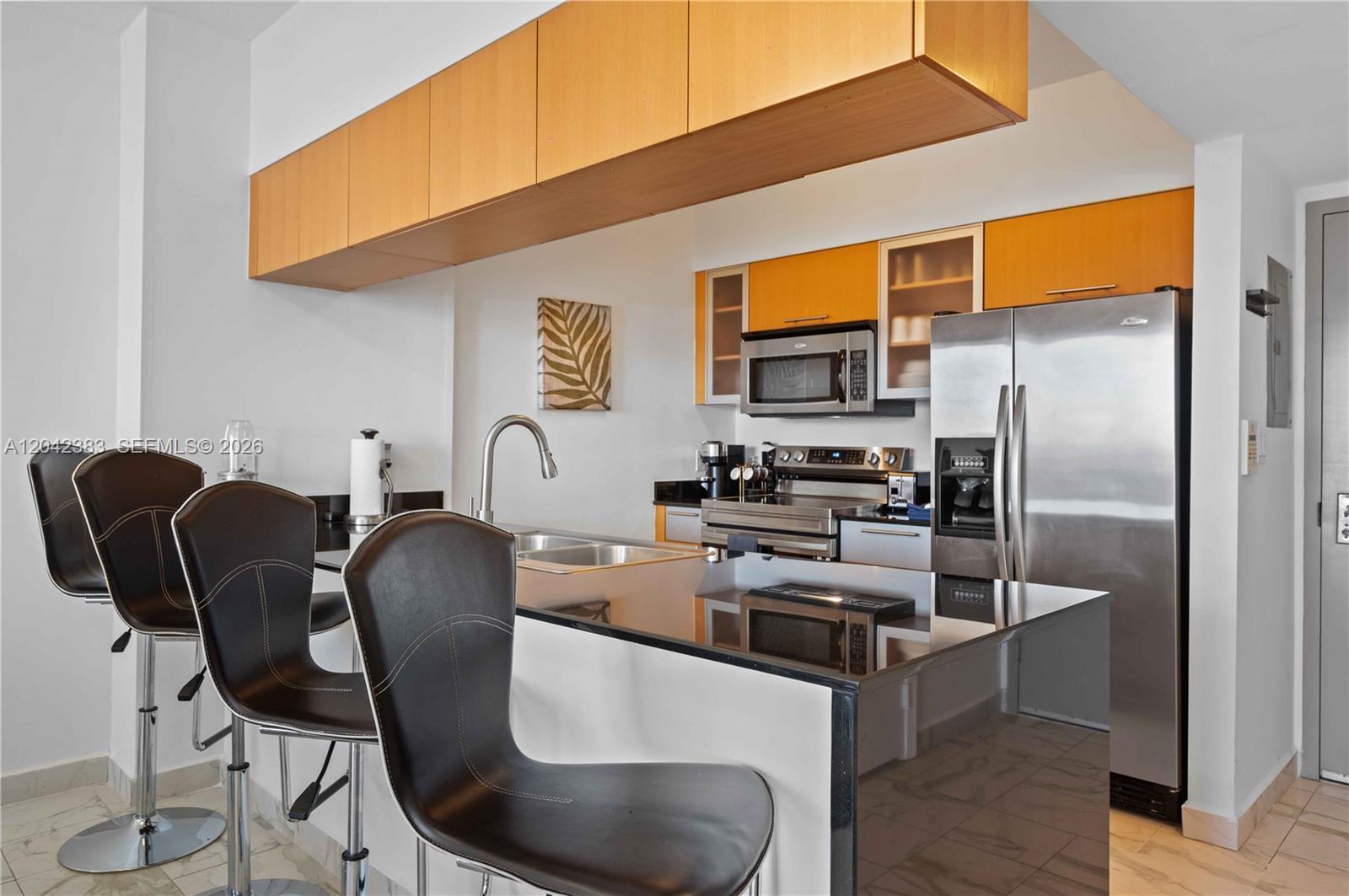 A kitchen features a black countertop island, bar stools, and light wood cabinetry — 1750 N Bayshore Dr # 5212, Miami FL 33132, MIAMI, FL