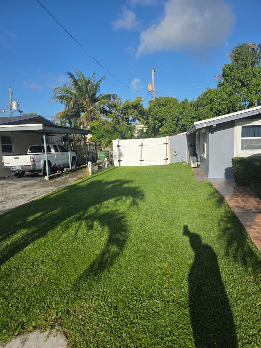 A grassy backyard features a white fence, a carport with a truck, and a house — 621 SW 56th Avenue, Margate FL 33068, MARGATE, FL
