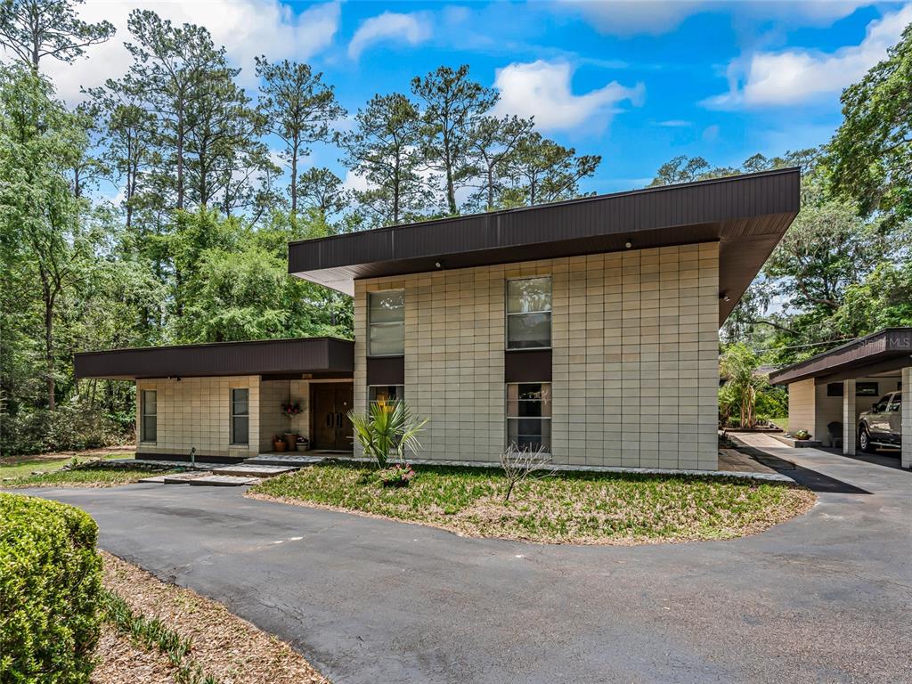 A two-story house with a flat roof and light-colored block exterior sits near trees — 2510 NW 30TH TERRACE, GAINESVILLE, FL