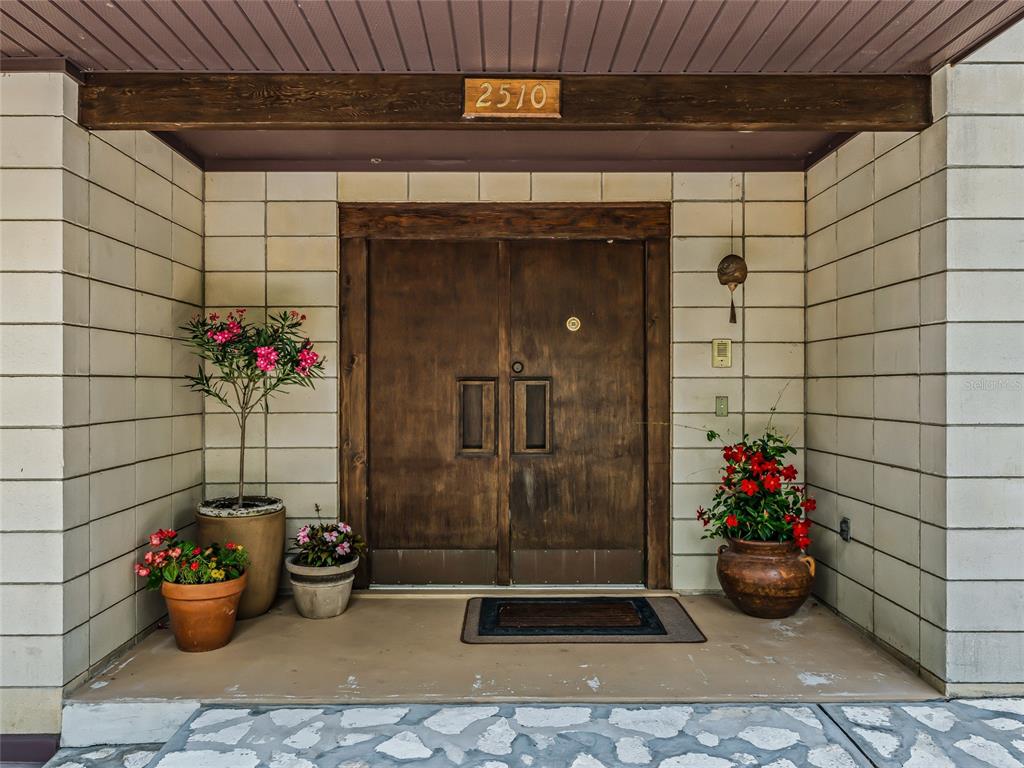 A double wooden front door with a house number above sits between two tiled walls — 2510 NW 30TH TERRACE, GAINESVILLE, FL