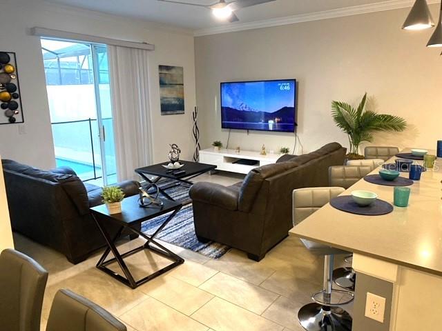 A living room with dark sofas, a television, and an adjacent kitchen island with stools — 4295 PARAGRAPH DRIVE, KISSIMMEE, FL