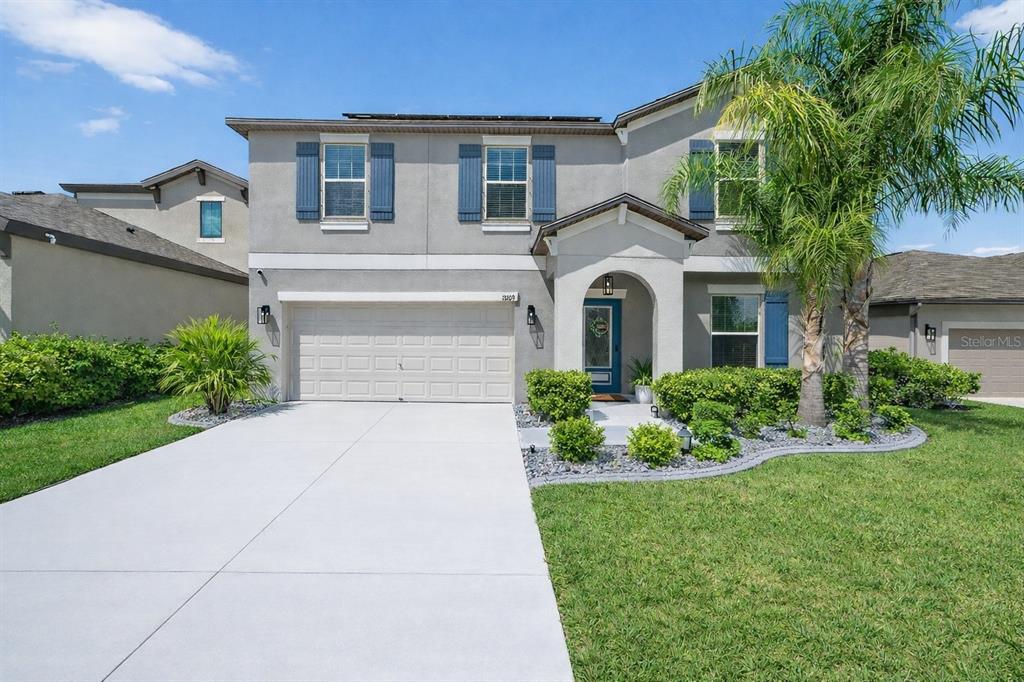 A two-story suburban house with a gray stucco exterior, blue shutters, and a concrete driveway — 13209 WILDFLOWER MEADOW DRIVE, RIVERVIEW, FL