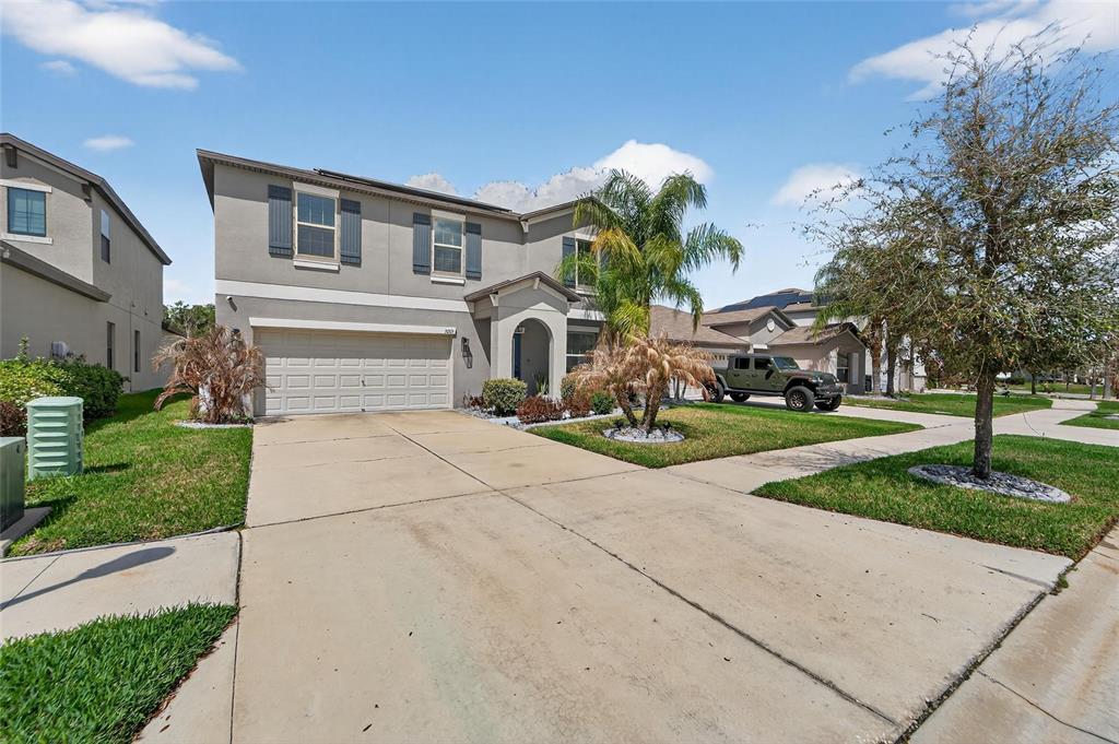 A two-story suburban house with a concrete driveway, a two-car garage, and a palm tree — 13209 WILDFLOWER MEADOW DRIVE, RIVERVIEW, FL