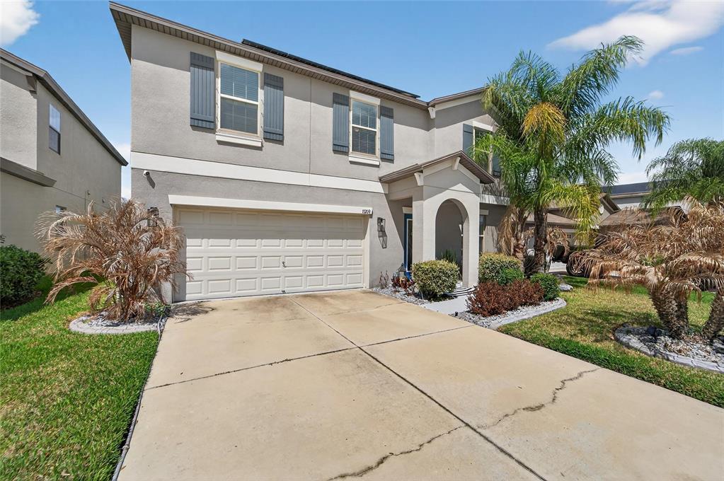 A two-story suburban house with a beige stucco exterior, a garage, and a palm tree — 13209 WILDFLOWER MEADOW DRIVE, RIVERVIEW, FL