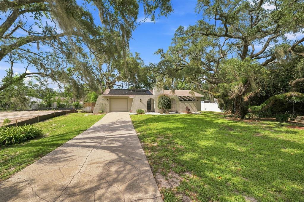 A single-story house with a concrete driveway, solar panels, and large oak trees in front — 400 FAIRBANKS ROAD, SPRING HILL, FL
