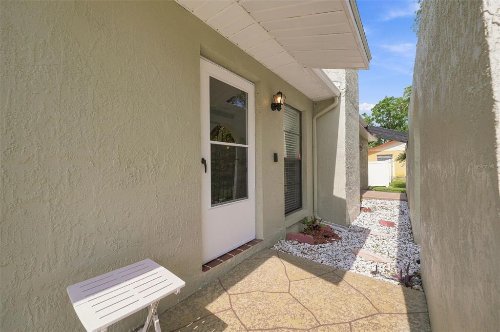 A white door with a storm door opens onto a small patio with stone pavers — 400 FAIRBANKS ROAD, SPRING HILL, FL