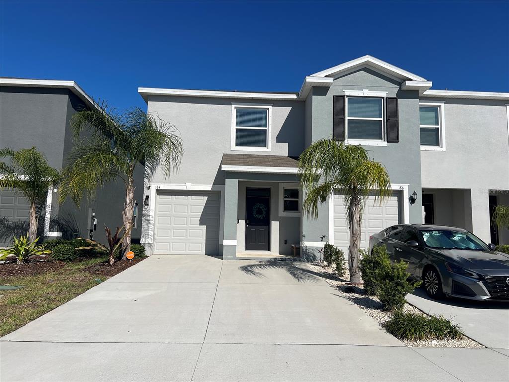 A two-story gray townhouse with two garage doors, palm trees, and a parked car — 184 MANGROVE SHADE CIRCLE, APOLLO BEACH, FL