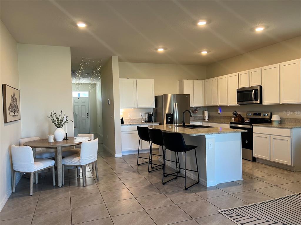 A kitchen with white cabinets, a granite island, and a dining area with a round table — 184 MANGROVE SHADE CIRCLE, APOLLO BEACH, FL