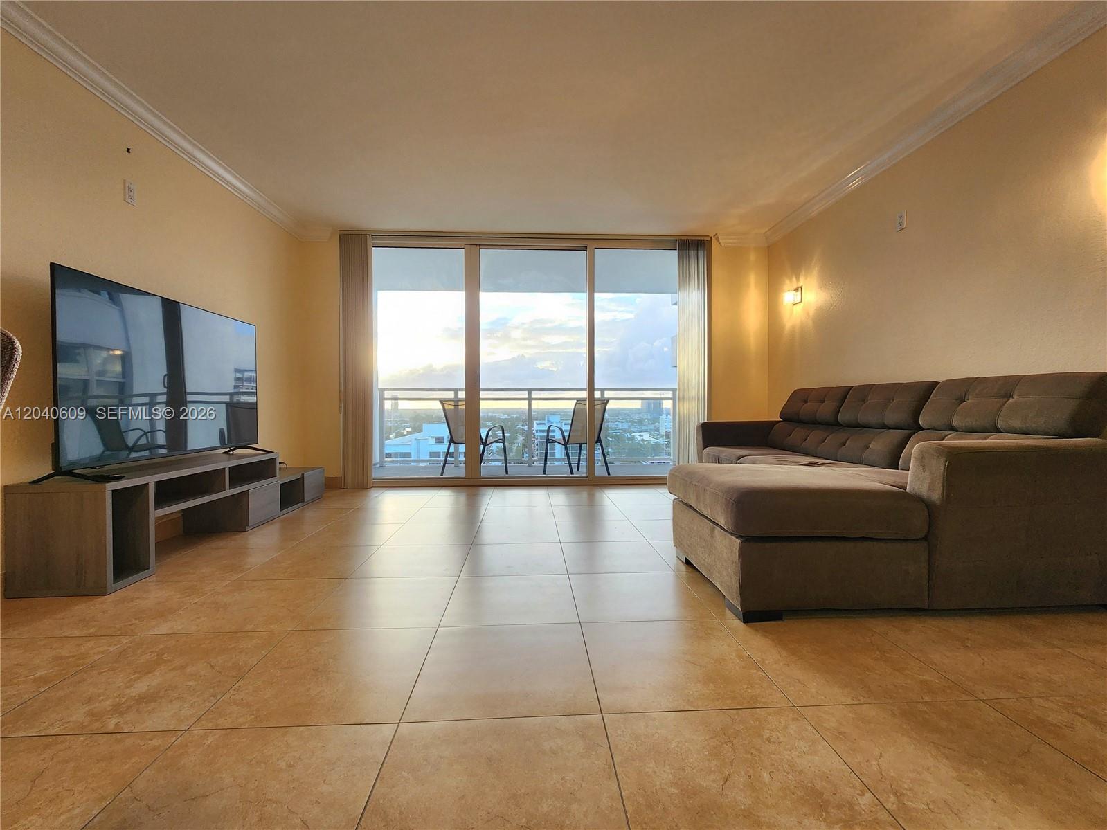A living room features tile flooring, a large sectional sofa, a television, and balcony access — 2030 S Ocean Dr # 1901, Hallandale Beach FL 33009, HALLANDALE BEACH, FL