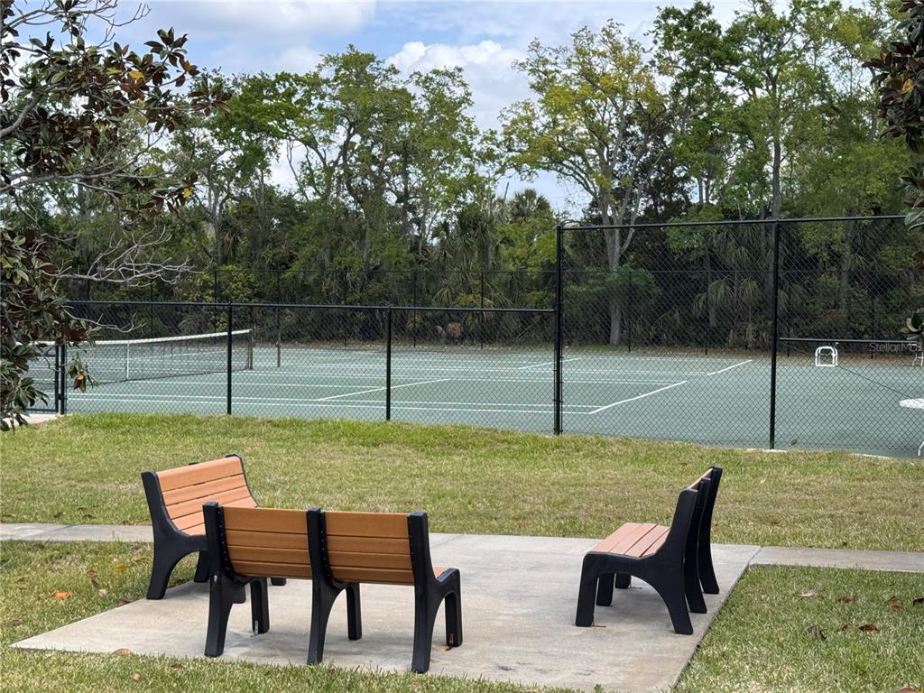 A concrete patio with three benches overlooks a fenced tennis court surrounded by trees — 1250 S PINELLAS AVENUE UNIT 804, TARPON SPRINGS, FL