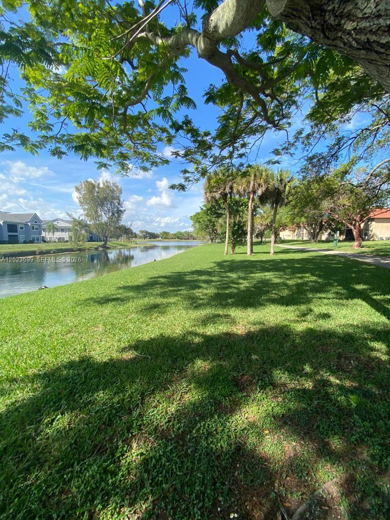 A grassy lawn slopes down toward a canal with palm trees and residential buildings nearby — 10370 SW 220th St # 224, Cutler Bay FL 33190, CUTLER BAY, FL