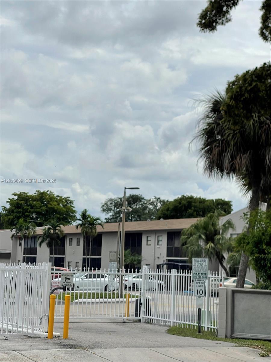 A white metal gate stands in front of a two-story apartment building with palm trees — 10370 SW 220th St # 224, Cutler Bay FL 33190, CUTLER BAY, FL