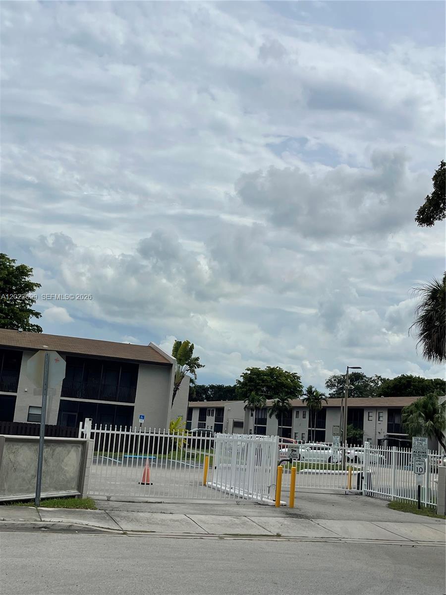 A gated entrance leads to a multi-story apartment complex under a cloudy sky — 10370 SW 220th St # 224, Cutler Bay FL 33190, CUTLER BAY, FL