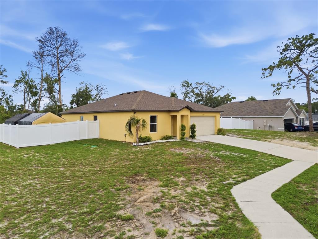 A yellow single-story house with a brown roof, two-car garage, and a white vinyl fence — 10198 ELGIN BOULEVARD, SPRING HILL, FL