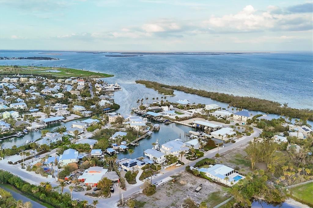An aerial view shows a coastal residential neighborhood with houses, canals, and a large bay — 140 DAMFINO STREET, BOCA GRANDE, FL