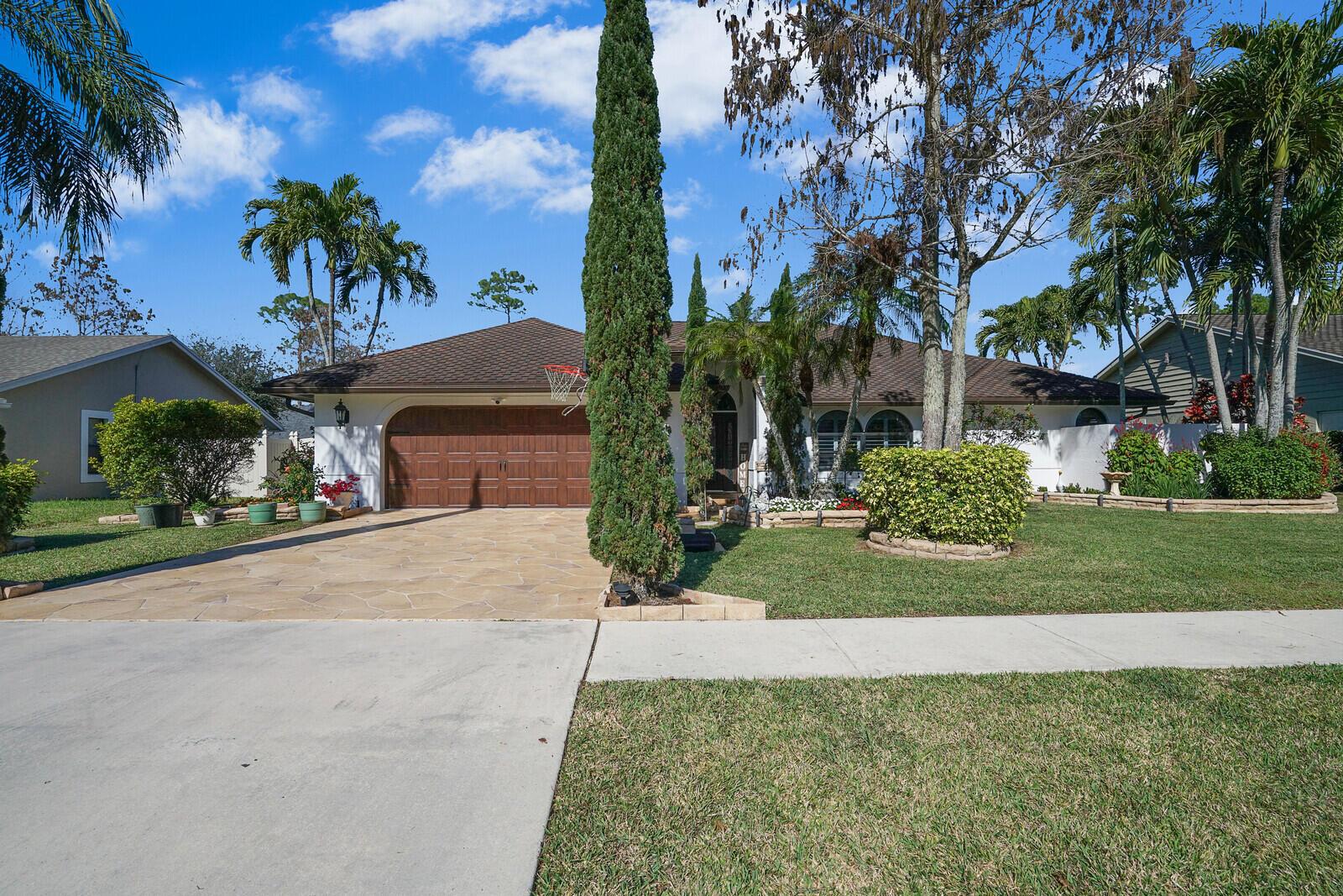 A single-story house with a brown garage door, stone driveway, and tall cypress tree — 1313 Brampton Cove, Wellington FL 33414, WELLINGTON, FL