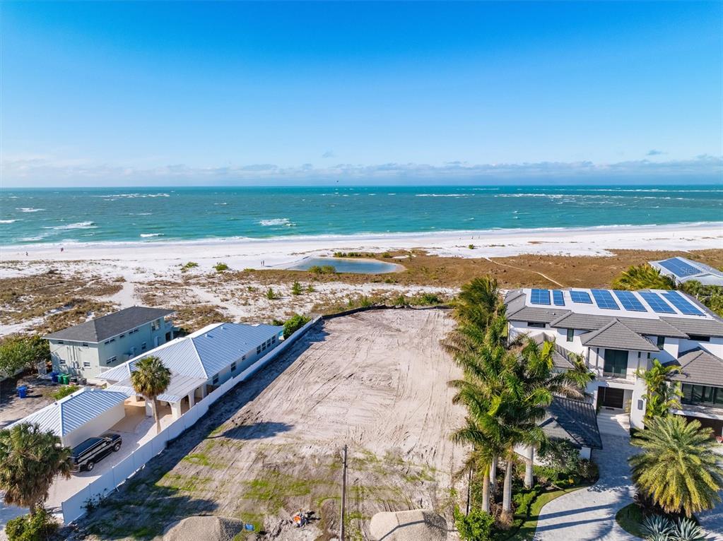 An aerial view shows a vacant beachfront lot situated between two modern houses — 769 N SHORE DRIVE, ANNA MARIA, FL