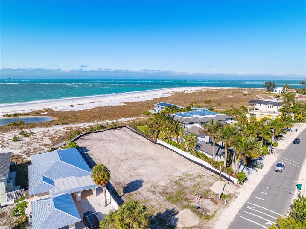 An aerial view shows a vacant beachfront lot situated between two houses and a road — 769 N SHORE DRIVE, ANNA MARIA, FL