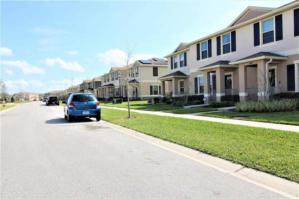 A street view of a residential neighborhood with townhouses and a parked blue car — 1842 KATZ CROSSING DRIVE, KISSIMMEE, FL