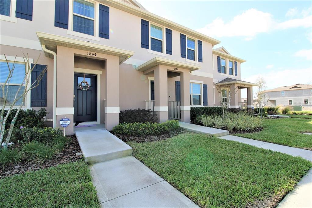 A row of multi-story townhouses features beige stucco siding, dark blue shutters, and covered entryways — 1842 KATZ CROSSING DRIVE, KISSIMMEE, FL