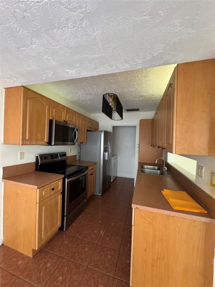 A galley-style kitchen features wood cabinets, laminate countertops, stainless steel appliances, and tiled flooring — 11405 SW 122nd Ct, Miami FL 33186, MIAMI, FL