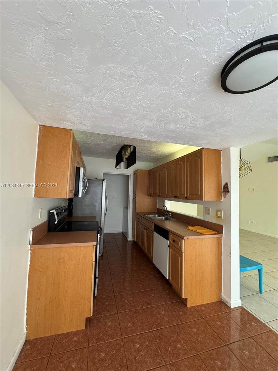 A galley kitchen features wood cabinets, brown countertops, and brown tile flooring — 11405 SW 122nd Ct, Miami FL 33186, MIAMI, FL