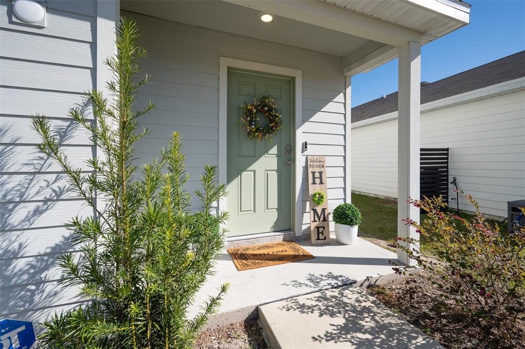 A light green front door with a wreath sits under a covered porch entrance — 1265 NW 248TH DRIVE, NEWBERRY, FL