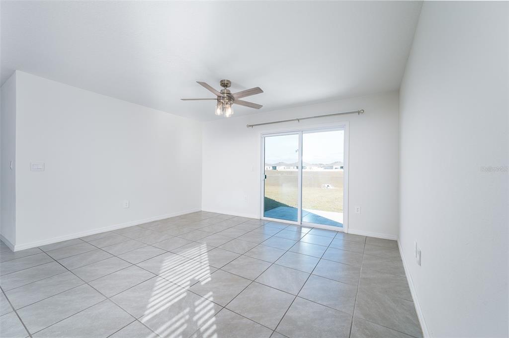 A bright, empty room features light gray tile flooring, a ceiling fan, and sliding glass doors — 1265 NW 248TH DRIVE, NEWBERRY, FL