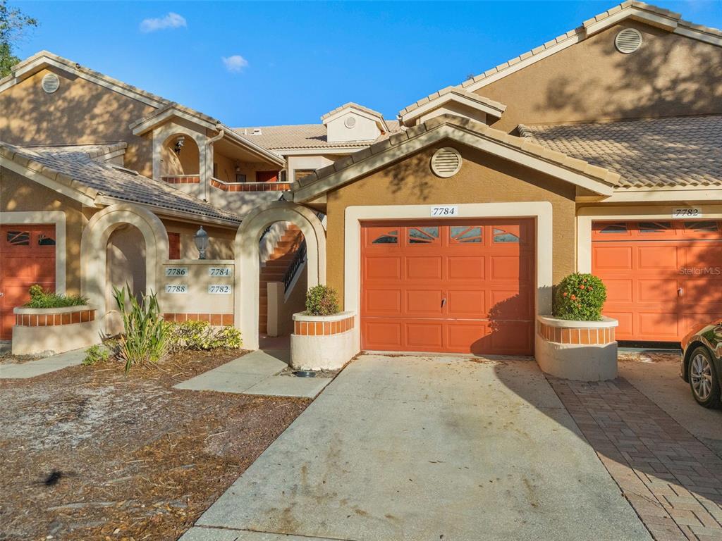 The exterior of a multi-unit residential building features stucco walls, orange garage doors, and tile roofs — 7784 SUGAR BEND DRIVE UNIT 7784, ORLANDO, FL